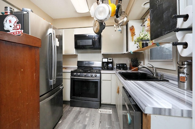 kitchen with white cabinetry, sink, light wood-type flooring, and appliances with stainless steel finishes