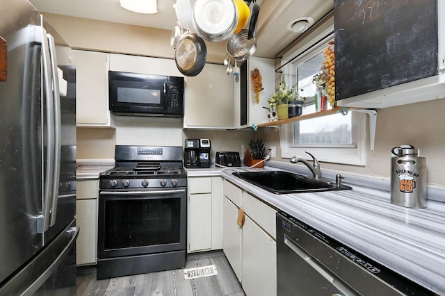 kitchen with white cabinets, appliances with stainless steel finishes, hardwood / wood-style floors, and sink