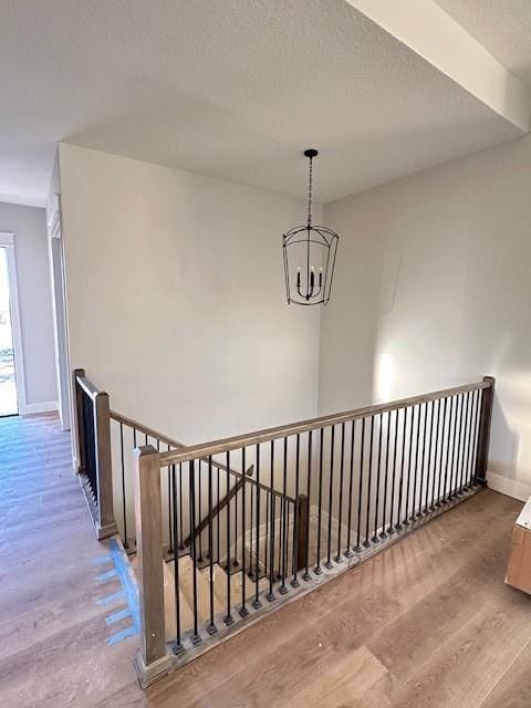 hallway with a textured ceiling, wood finished floors, an upstairs landing, baseboards, and an inviting chandelier