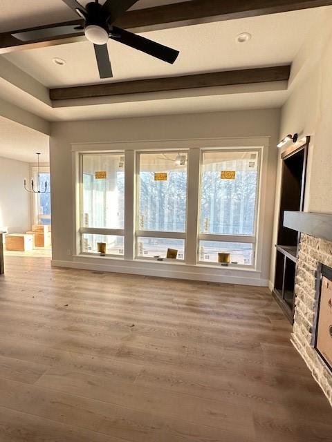 unfurnished living room featuring ceiling fan, beamed ceiling, a fireplace, and wood finished floors