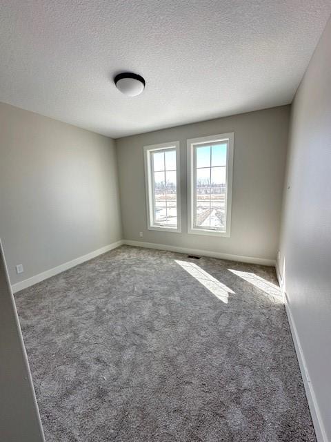 empty room featuring a textured ceiling, carpet floors, and baseboards