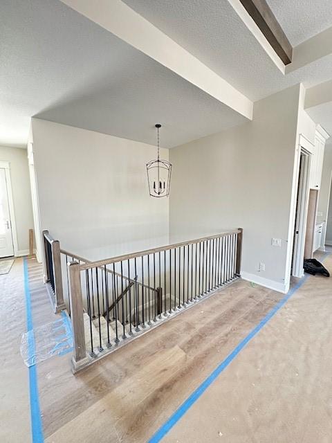 corridor featuring baseboards, a notable chandelier, a textured ceiling, and an upstairs landing