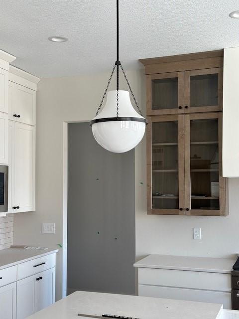 kitchen featuring glass insert cabinets, light countertops, white cabinets, and decorative light fixtures