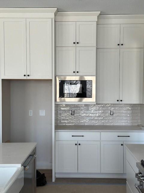 kitchen with tasteful backsplash, baseboards, stainless steel microwave, light countertops, and white cabinetry