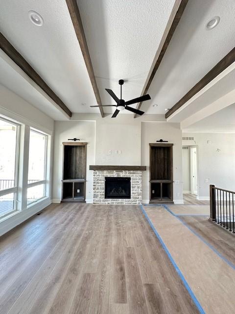 unfurnished living room with light wood-style floors, a fireplace, baseboards, and beam ceiling