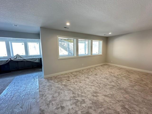 carpeted spare room featuring recessed lighting, a healthy amount of sunlight, a textured ceiling, and baseboards