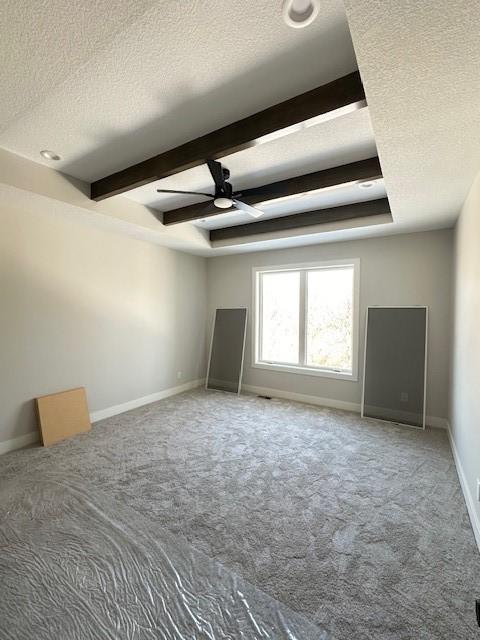 interior space featuring a raised ceiling, ceiling fan, a textured ceiling, beamed ceiling, and baseboards