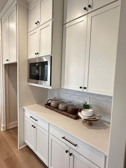 703 Richland Ct, Van Meter, IA 50261 - kitchen with tasteful backsplash, wood finished floors, stainless steel microwave, light countertops, and white cabinets