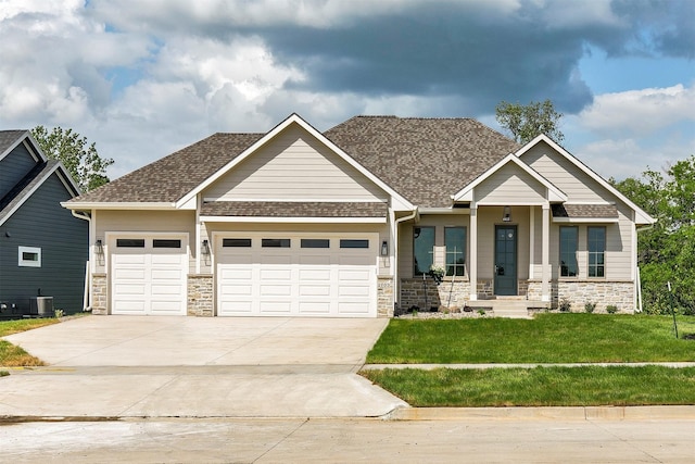 703 Richland Ct, Van Meter, IA 50261 - craftsman house with an attached garage, driveway, a front lawn, roof with shingles, and stone siding