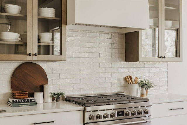 703 Richland Ct, Van Meter, IA 50261 - kitchen featuring high end stainless steel range, premium range hood, light countertops, backsplash, and glass insert cabinets