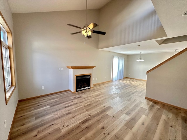 unfurnished living room featuring ceiling fan with notable chandelier, light wood-type flooring, and high vaulted ceiling