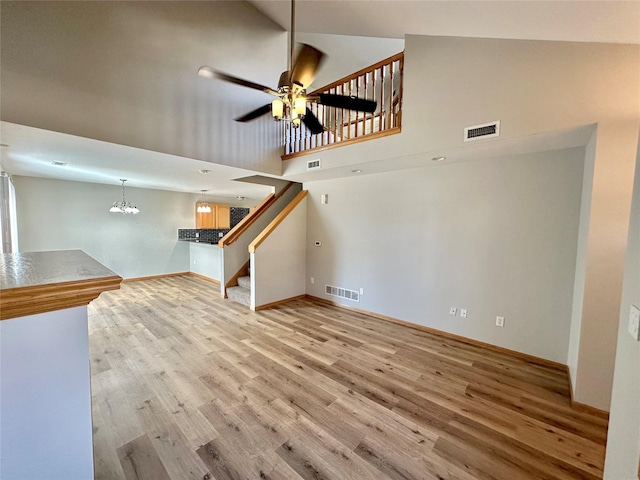 unfurnished living room featuring ceiling fan with notable chandelier, light hardwood / wood-style floors, and high vaulted ceiling