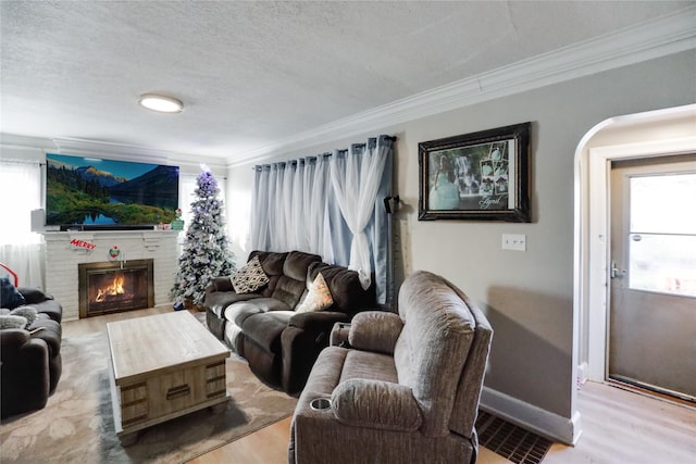 living room with hardwood / wood-style floors, a textured ceiling, a brick fireplace, and crown molding