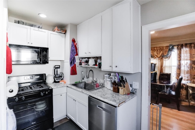 kitchen with light stone counters, dark wood-type flooring, sink, black appliances, and white cabinetry