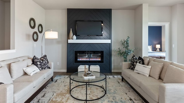 living area with a large fireplace, baseboards, and wood finished floors