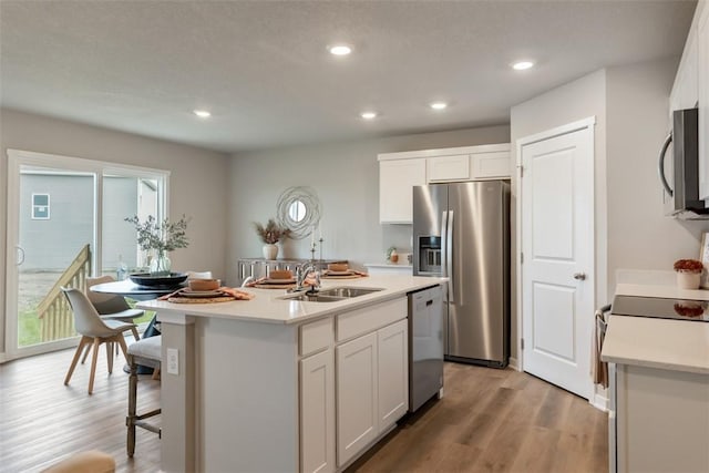 kitchen with a sink, light wood-type flooring, light countertops, appliances with stainless steel finishes, and a kitchen island with sink