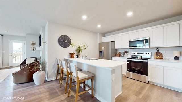 kitchen with white cabinets, appliances with stainless steel finishes, light hardwood / wood-style flooring, and a kitchen breakfast bar