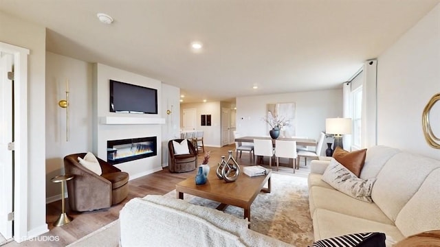 living room featuring a glass covered fireplace, baseboards, recessed lighting, and wood finished floors