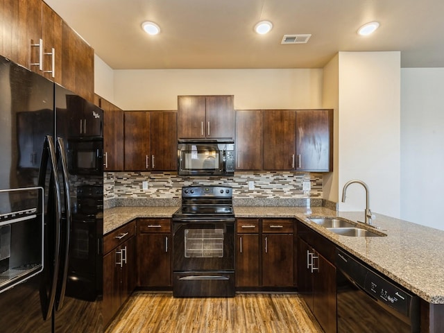 kitchen featuring light stone countertops, sink, kitchen peninsula, black appliances, and light wood-type flooring