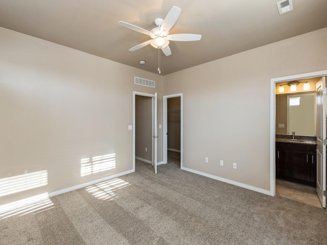 unfurnished bedroom with ceiling fan, light colored carpet, a spacious closet, and ensuite bath