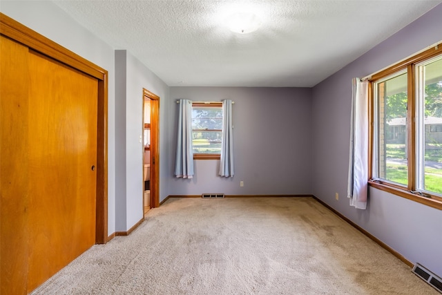 unfurnished bedroom with a textured ceiling, light carpet, and a closet