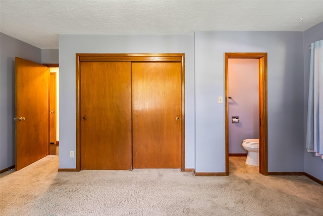 unfurnished bedroom with ensuite bath, a closet, light colored carpet, and a textured ceiling