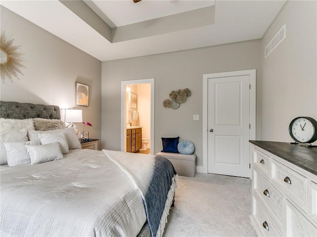 bedroom featuring a raised ceiling, ensuite bath, and light colored carpet