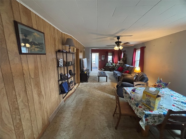 dining space featuring light carpet, ceiling fan, and wooden walls