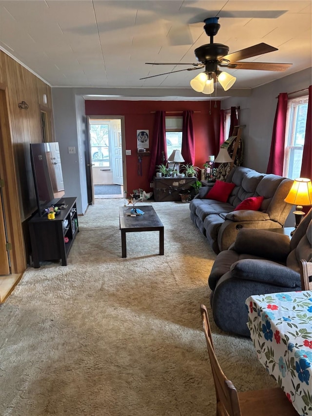 living room featuring carpet flooring, wood walls, ceiling fan, and a healthy amount of sunlight