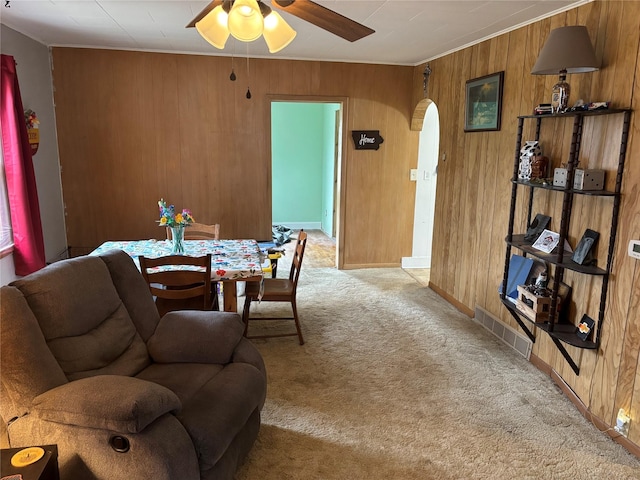 dining area with light carpet, ceiling fan, and wooden walls