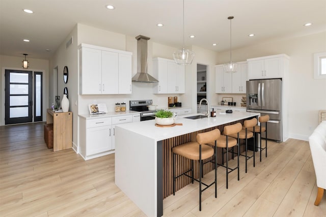 kitchen with sink, white cabinetry, stainless steel appliances, a kitchen island with sink, and wall chimney range hood