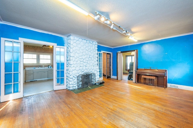 unfurnished living room with a stone fireplace, wood-type flooring, crown molding, and french doors