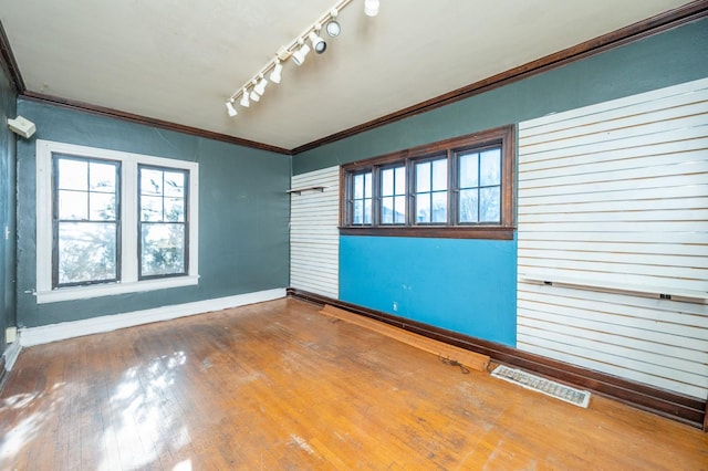 empty room featuring rail lighting, hardwood / wood-style flooring, and ornamental molding