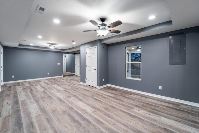 basement featuring a textured ceiling, electric panel, and light hardwood / wood-style flooring