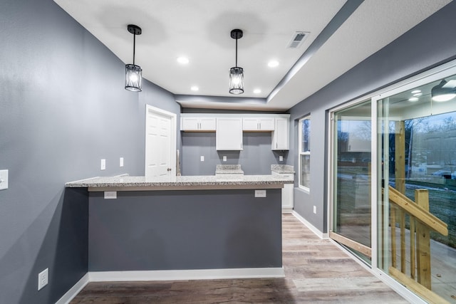 kitchen featuring kitchen peninsula, white cabinetry, pendant lighting, and light wood-type flooring