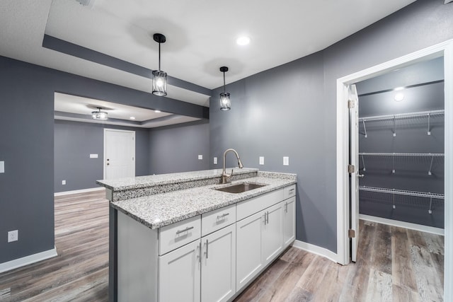 kitchen featuring sink, light stone counters, hardwood / wood-style floors, pendant lighting, and white cabinets