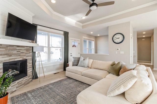 living room featuring a raised ceiling, a tiled fireplace, ceiling fan, and light hardwood / wood-style floors