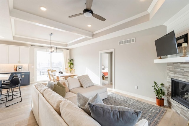 living room featuring a tray ceiling, a tiled fireplace, ceiling fan, and light hardwood / wood-style flooring