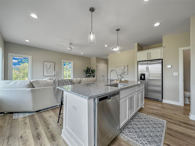 kitchen with white cabinets, stainless steel appliances, a center island with sink, and sink