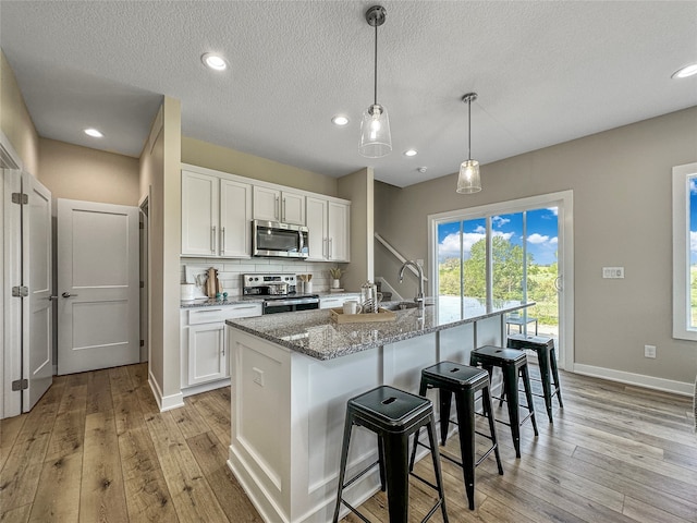 kitchen featuring light stone countertops, white cabinetry, stainless steel appliances, a center island with sink, and light wood-type flooring