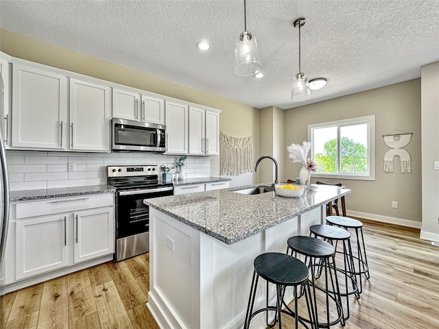 kitchen with white cabinets, a center island with sink, sink, decorative light fixtures, and stainless steel appliances