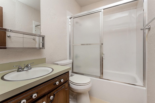 full bathroom with vanity, toilet, a textured wall, and bath / shower combo with glass door