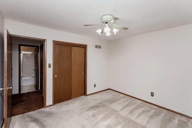 unfurnished bedroom featuring baseboards, visible vents, a closet, a textured ceiling, and light carpet