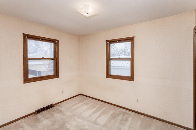 spare room featuring visible vents, light colored carpet, wallpapered walls, and baseboards