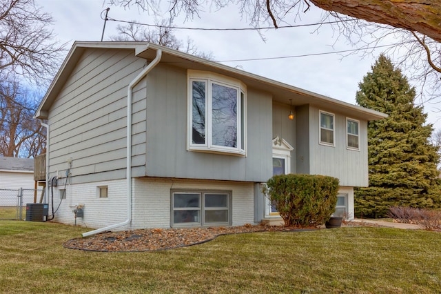 bi-level home featuring cooling unit, brick siding, a front yard, and fence