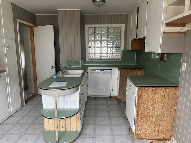 kitchen with dishwasher, backsplash, sink, wooden walls, and white cabinetry