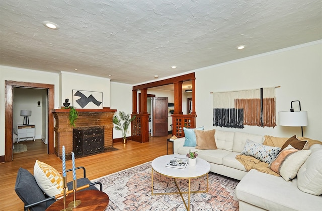 living room featuring hardwood / wood-style flooring, ornamental molding, a brick fireplace, and a textured ceiling