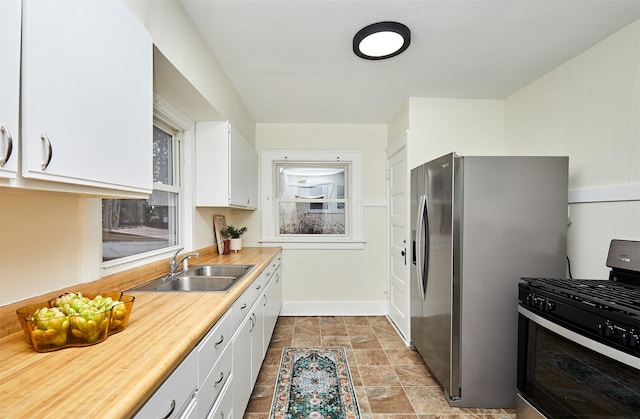 kitchen with sink, gas range, stainless steel fridge, and white cabinets