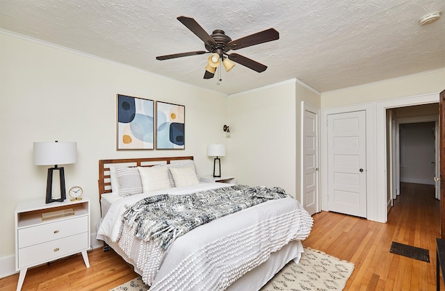 bedroom with ceiling fan, ornamental molding, light hardwood / wood-style floors, and a textured ceiling