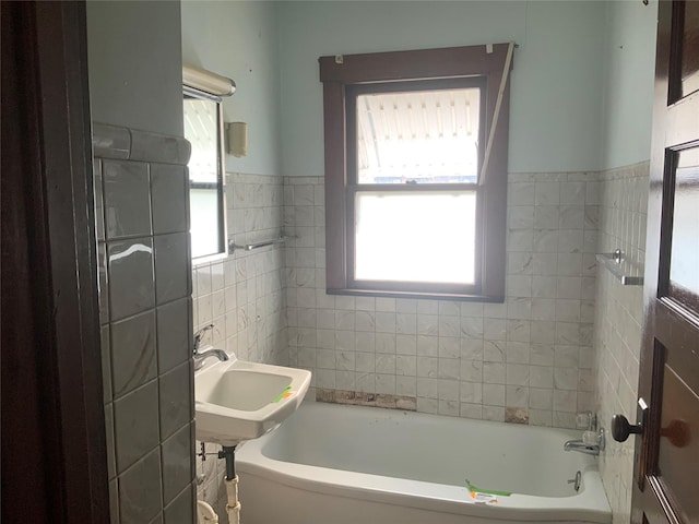 bathroom featuring sink, a tub to relax in, and tile walls